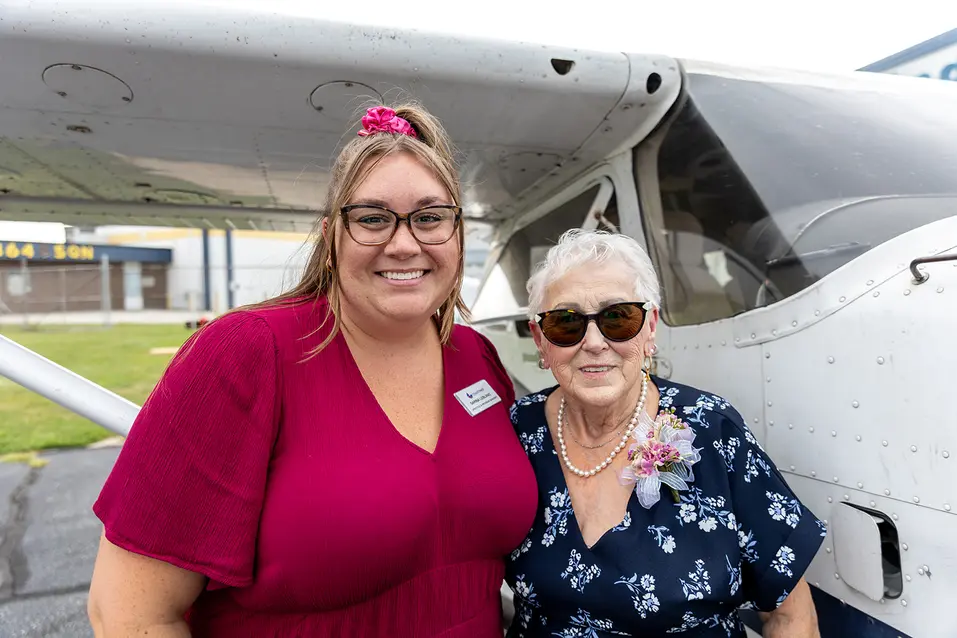 Shirley, a resident of Chartwell Oak Park Terrace, posing with a team member beside a small aircraft.
