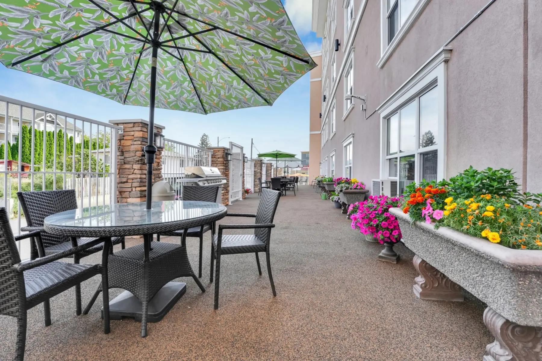 Exterior patio at Chartwell Kamloop with parasol table, chairs and flower beds / Terrasse extérieure de Chartwell Kamloop avec table parasol, chaises et parterres de fleurs