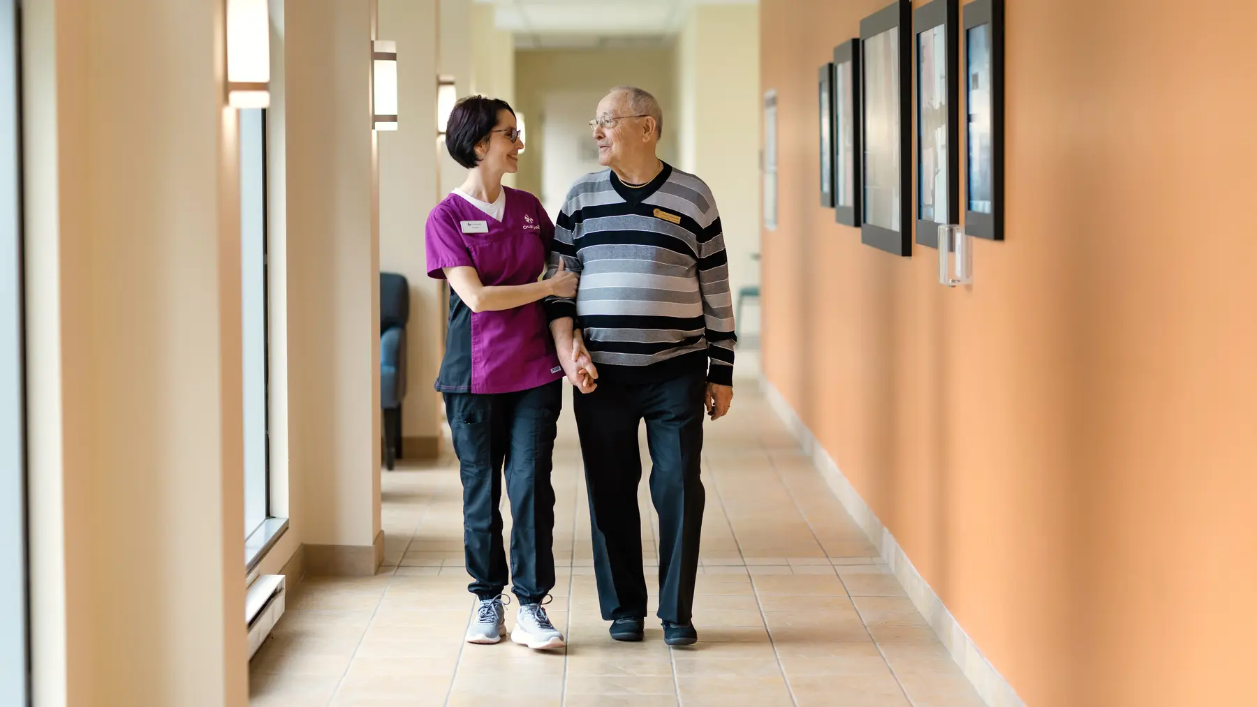 Chartwell staff is assisting senior male resident walking down an aisle / Le personnel de Chartwell aide un résident âgé à marcher dans l'allée