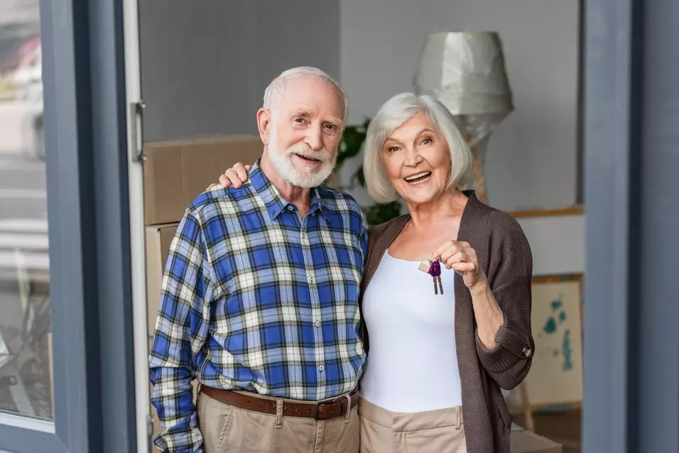 laughing senior woman holding keys and embracing husband in new house