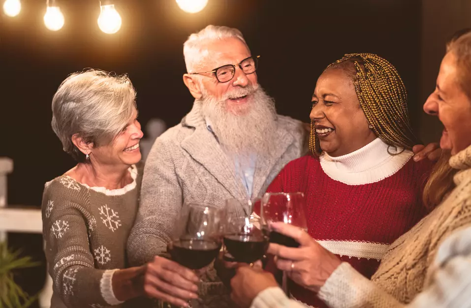 A group of seniors are toasting their wine glasses with a big joyous smiles during a holiday party